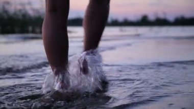 Kız su üzerinde günbatımında yürür.