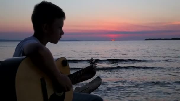 Niño juega en la guitarra al atardecer — Vídeo de stock