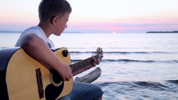 Pojke spelar på gitarr vid solnedgången — Stockvideo