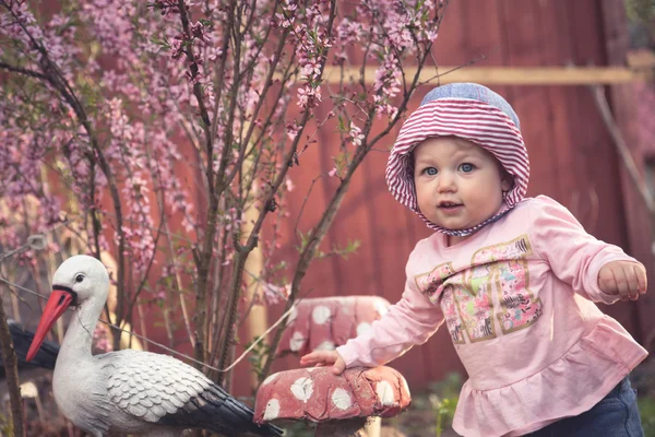 Мила маленька дівчинка в рожевій сукні, що має камеру в парку. Квітуче дерево і лелека на фоні — стокове фото