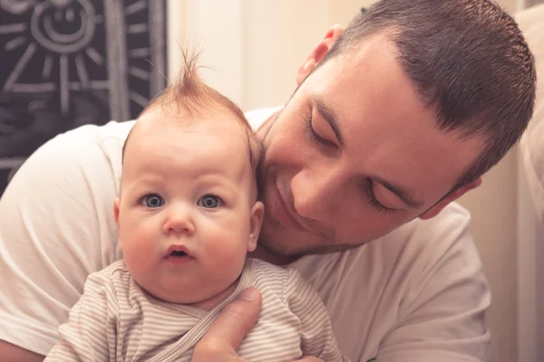 Father embracing his little baby. Father is looking on baby, baby is looking on camera. Baby with funny haircut — Stock Photo, Image