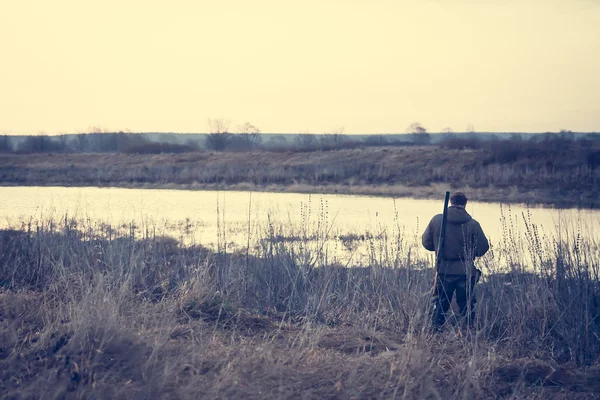 猎人男人站在河岸边朦胧日出时在农村领域的成功捕猎的期望 — 图库照片