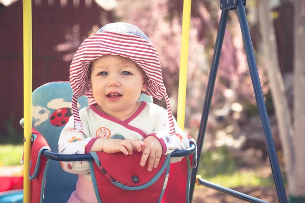 Schattige kleine baby zittend op schommels tijdens zonnige zomerdag in het park Stockafbeelding