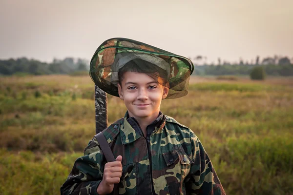 Giovane ragazzo sorridente con fucile da caccia in piedi al campo verde durante il tramonto — Foto Stock