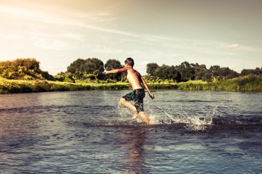 Nehir kıyısında günbatımı sırasında ileri çalışan genç çocuk