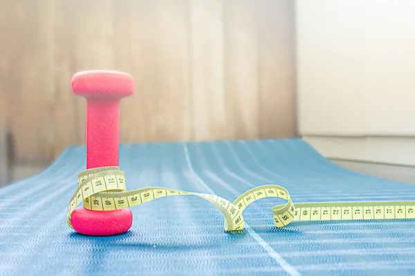 Centimeter tape around a dumbbell on a yoga mat. Weight loss concept — Fotografia de Stock