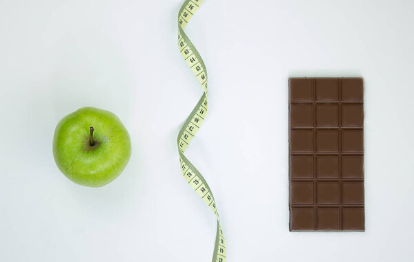 Choose between a healthy lifestyle and junk food. Apple centimeter ribbon and chocolate on a white background