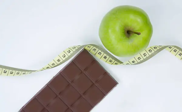 Choose between a healthy lifestyle and junk food. Apple centimeter ribbon and chocolate on a white background — Fotografia de Stock