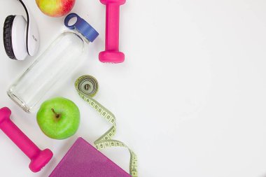 Two red dumbbells, an apple, a tape measure, a bottle of water and weight scales on a white background. Concepts about fitness, sport and health. Copy space for text. Home workout concept