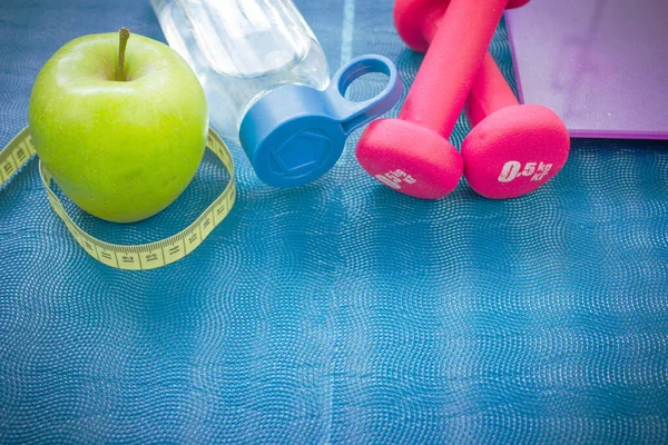 Two red dumbbells, an apple, a tape measure, a bottle of water and weight scales on a yoga mat. Concepts about fitness, sport and health — Fotografia de Stock