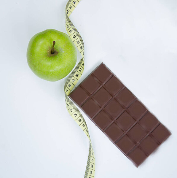 Choose between a healthy lifestyle and Junk food. Apple centimeter ribbon and chocolate on a white background