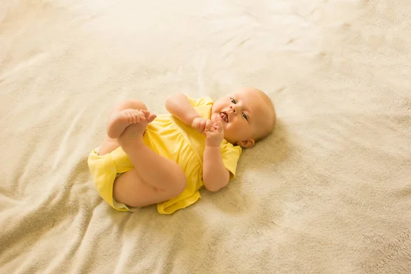 Carina, dolce e affascinante bambina con un body giallo sdraiata sul letto e sorridente. — Foto Stock