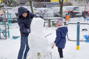 Yetişkinler ve çocuklar karlı oyun sahasında bir kardan adam yaratıyor..