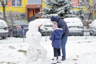 Bir çocuk ve bir yetişkin dışarıda kardan adam yapıyor..