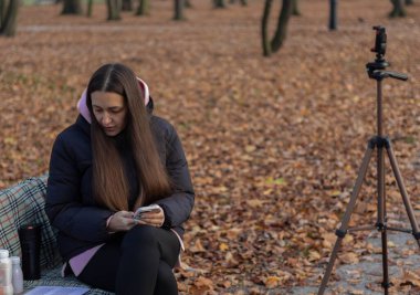 Blogcu bir bankta notları gözden geçiriyor, açık havada canlı yayın oturumuna başlamaya hazır.