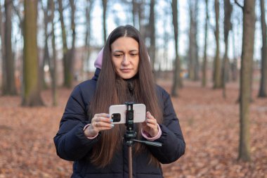 Blogcu, sonbaharda canlı yayın için telefon hazırlıyor, park manzarası yakalıyor.
