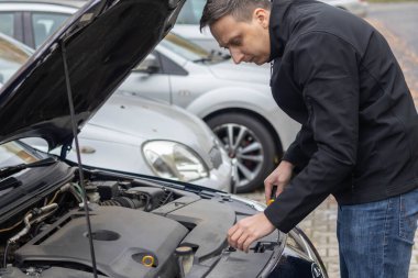 Adam park halindeki araçlarla çevrili bir araç kullanarak motor kapağını inceler.