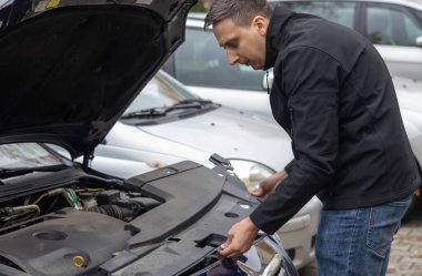 Bir adam motoru park alanındaki bir aracın motoruna yerleştirir..