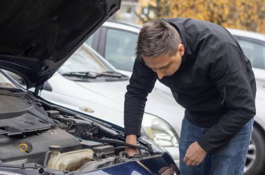 Adam bir aracın motor bölmesini inceleyip düşük ışın parçası arıyor..