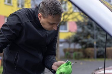 Adam bir çubuğu siliyor ve bakım alanındaki bir araba motorunun yağ seviyesini kontrol ediyor..
