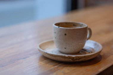 Seramik bir fincan, ahşap bir masanın üzerinde, içinde yumuşak bir ışık olan bir tabağın üzerinde duruyor..