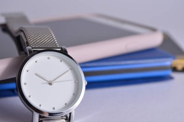 Beyaz bir arka planda kadın saati, telefon ve not defteri..