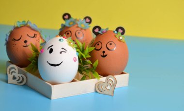 Sarı-mavi arka planda bir kutuda komik yüzlü Paskalya yumurtaları. Paskalya.
