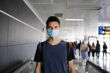 Coronavirus genç beyaz adam havaalanında maske takıyor. Covid-19 seyahat konsepti. Halka açık bir alanda sırt çantalı genç bir gezgin. Küresel bir salgın sırasında yurtdışında okumak. Corona koruması.