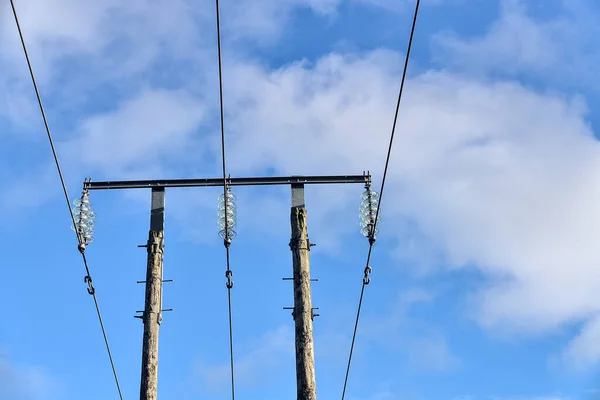 Overhead electrical power lines on old wooden pillar captured against the blue sky with soft white clouds in Co. Dublin, Ireland. Three voltage wires