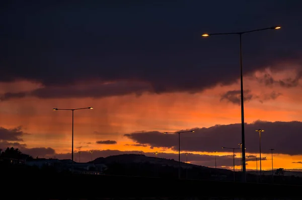 Spectacular red sunset with dark rainy clouds over the bridge with silhouettes of people and vehicles and tall street lanterns along highway M50 in Dublin, Ireland. Beautiful cold sunset clouds