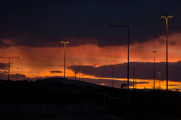 Spectacular red sunset with dark rainy clouds over the bridge with silhouettes of people and vehicles and tall street lanterns along highway M50 in Dublin, Ireland. Beautiful cold sunset clouds
