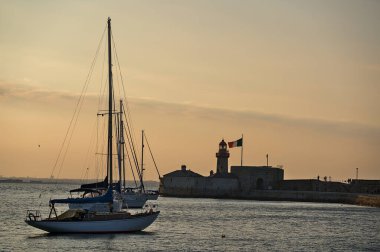 Dublin, İrlanda - 21 Haziran 2021: Dun Laoghaire limanında İrlanda bayrağı taşıyan kırmızı Doğu İskelesi feneri yakınlarında demirleyen yelkenlilerin güzel akşam manzarası. Yumuşak ve seçici odak