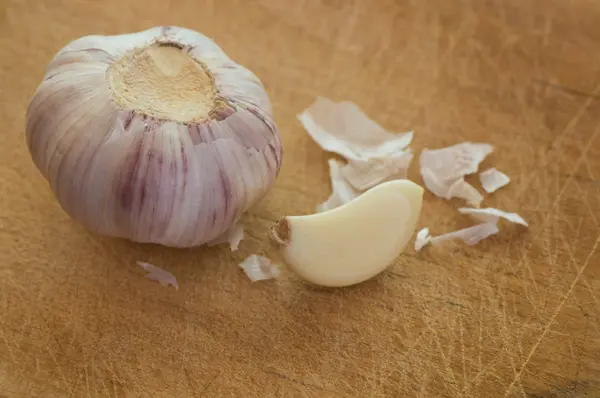 Whole garlic head with peeled garlic segment on a used wooden cutting board — Stock Photo, Image