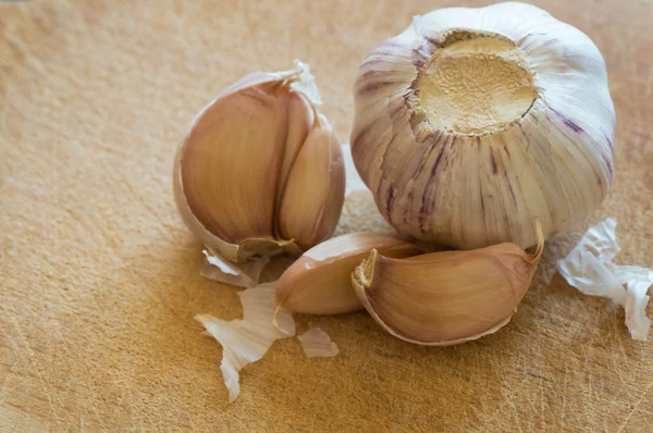 Whole garlic head and segments of garlic on a used wooden cutting board — Stock Photo, Image