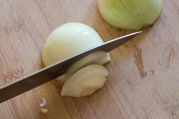 Peeled yellow onion half being sliced with a knife on a used wooden cutting board — Stock Photo, Image