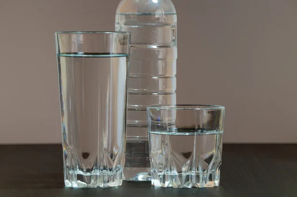 Two different height glass containing clean water and a plastic bottle of water in between