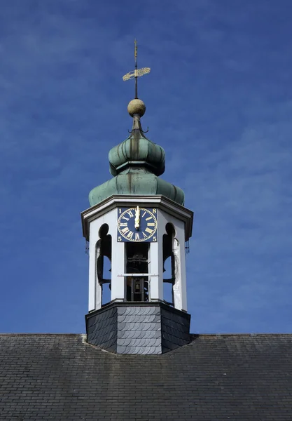 Old church tower with golden clock and green roof. Weather vane on top of the roof. Composition of white, black, gold and mint green. It\'s twelve o\'clock. Blue sky