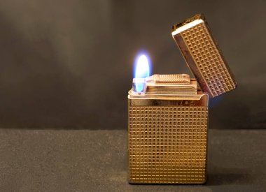 Eskimiş altın rengi çakmak, kahverengi arka planda çıkıntılar ve alevlerle çizikler var..  