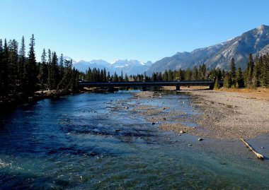 Banff, Alberta, Kanada 'daki Bow Nehri' nin inanılmaz mavi suları. Sağ kıyıda çakıl taşları. Köprü, orman ve uzaktaki etkileyici kayalıklar. Rüya gibi bir manzara.