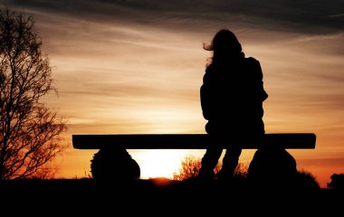 Güneş doğarken bankta oturan bir kadının silueti.