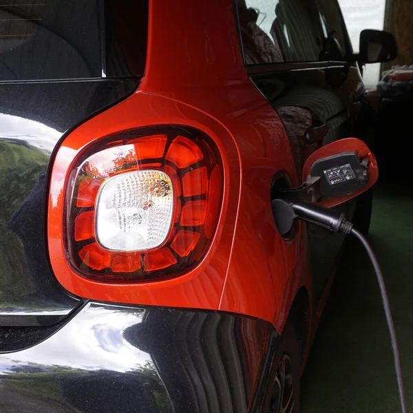 Charging a black and red electric car at home with an  electro charging station. One back light and the charging power plug. Environmentally conscious recharging of an electric vehicle.
