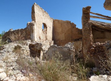 A completely dilapidated stone house in the Spanish sunshine. Nature takes over. A ruin in a very dry landscape. The sky is cloudless blue. 