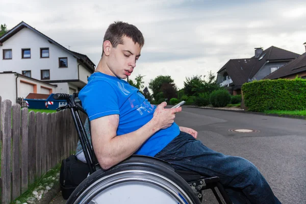 Garçon handicapé avec smartphone attendant le bus scolaire — Photo