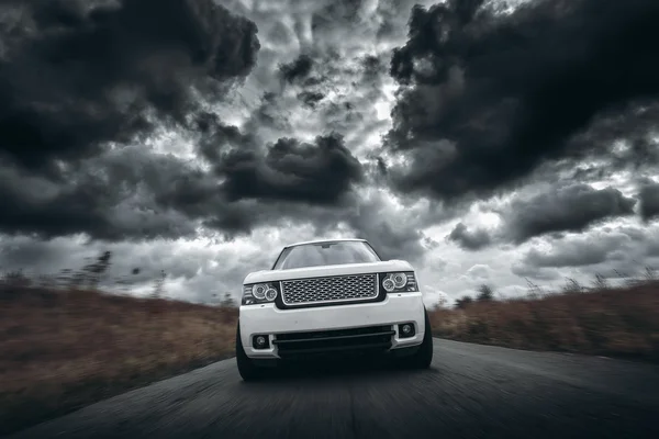 Velocidade do carro branco dirigindo na estrada em nuvens dramáticas durante o dia — Fotografia de Stock