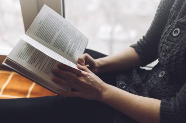 Kadın pencere yakınındaki ekose koltukta kitap okumak
