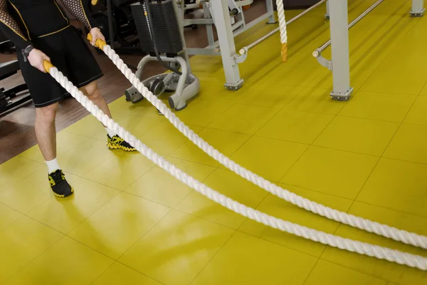 Man training with battle rope in fitness club