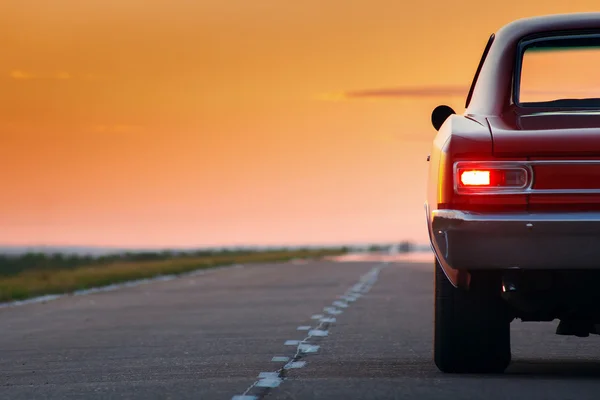 Retro červené auto pobyt na asfaltovou silnici při západu slunce — Stock fotografie