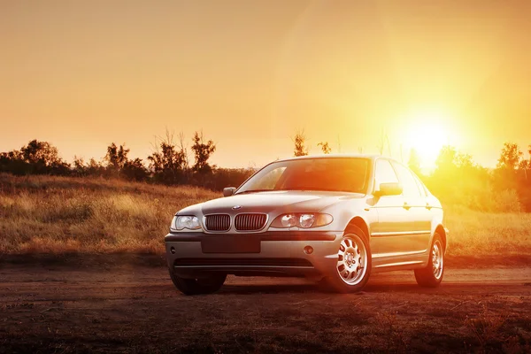 Bil Bmw E46 vistelse på landsbygden road vid solnedgången — Stockfoto