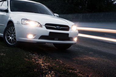 Araba Subaru Legacy alacakaranlıkta geçen araçların yakınında asfalt yolda kalmak