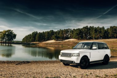 Araba Land Rover Range Rover gündüz göl ve orman yakınında kum üzerinde durmak